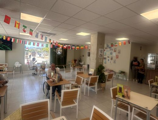 Imagen del interior de la cafetería. En una de las mesas hay una persona usuaria de silla de ruedas.