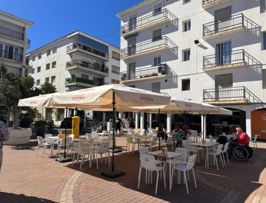 Imagen de la terraza del bar con grandes sombrillas. En una delas mesas hay una persona usuaria de silla de ruedas.