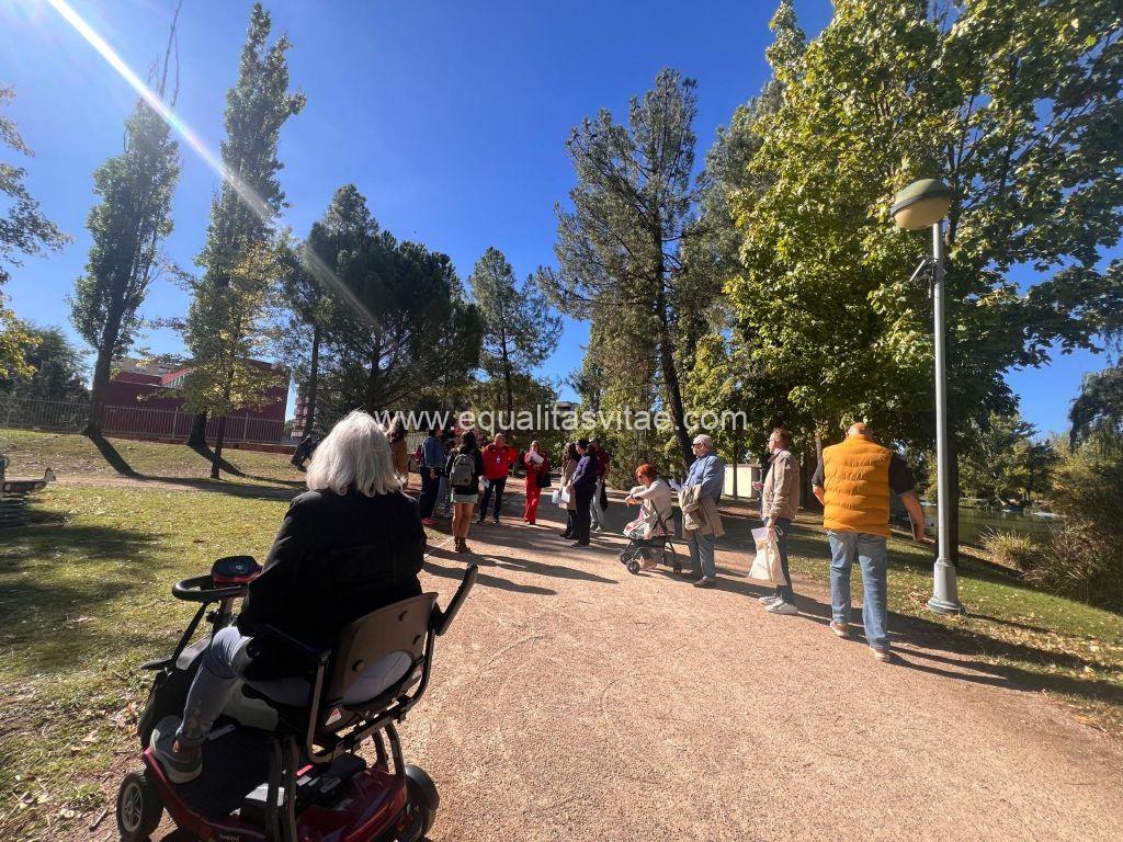 Imagen de un grupo de personas en un parque con sendero de tierra compacta rodeado de zona ajardinada. Varias personas van en silla de ruedas.