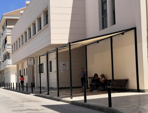Imagen de la fachada principal del centro de salud de Altea. Hay varias personas junto a la entrada, una de pie y dos sentadas en un banco.