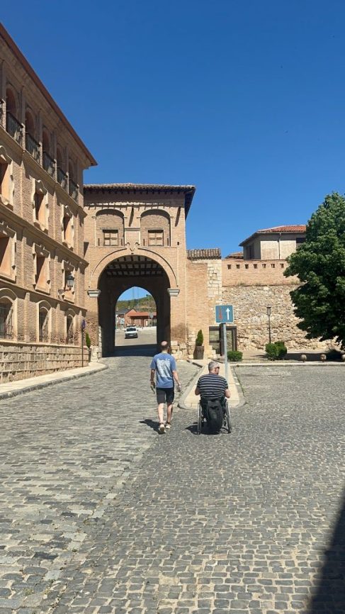 Imagen de dos personas acercándose al arco de entrada al casco histórico de Daroca, una de ellas va en silla de ruedas.