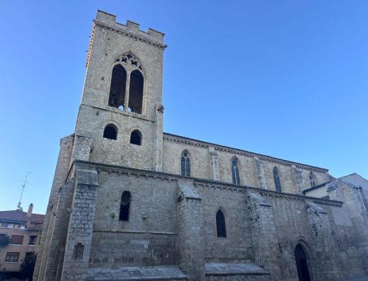 Imagen de la fachada lateral de la iglesia. A la izquierda la torre. Los muros son de piedra y las ventanas son estrechas con arcos apuntados.