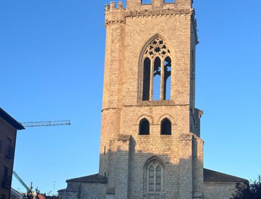 Imagen de la fachada principal de la iglesia dominada por su gran torre campanario de piedra, de planta cuadrada y aspecto defensivo.