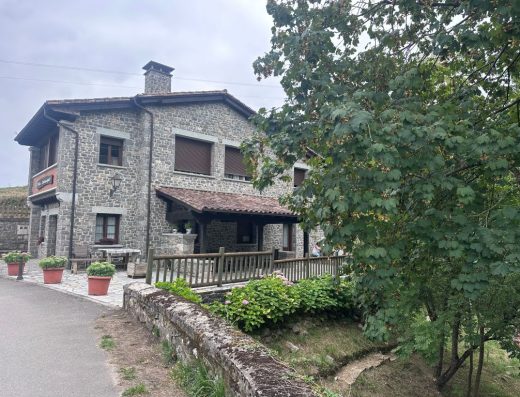 Imagen panorámica de una casa rústica con fachada de piedra. Tejado a dos aguas.